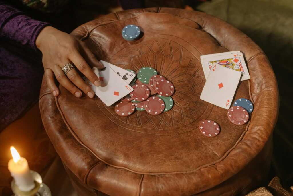 A hand playing cards on a leather table with poker chips and a candle.