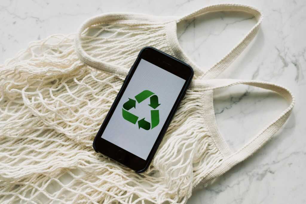 Mesh bag with smartphone displaying recycle symbol, promoting sustainability.
