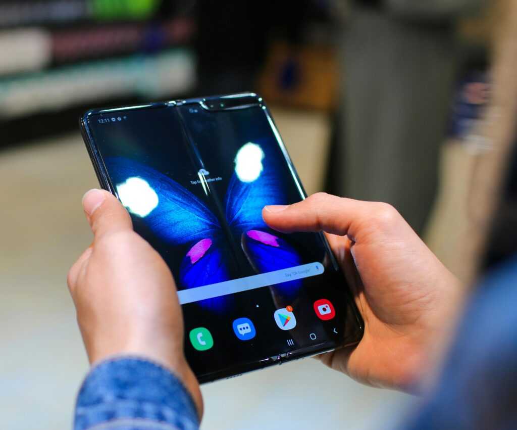 Close-up of hands holding a foldable smartphone showing a butterfly on the screen.