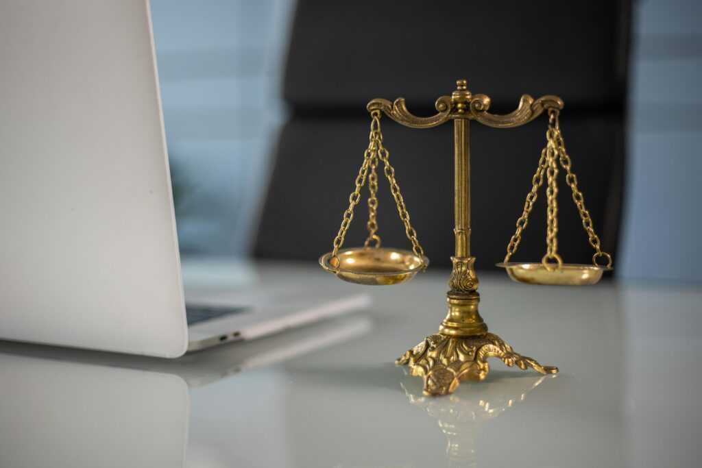 Golden justice scales on a desk beside a laptop, symbolizing law and balance.